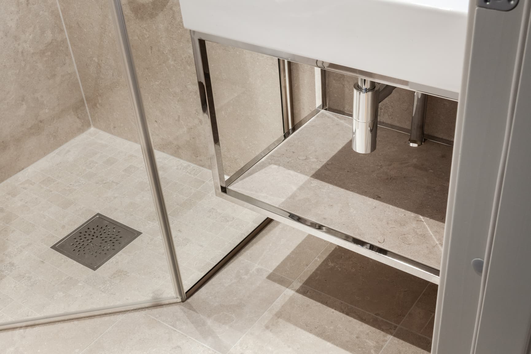 Detaljbilde av baderomsgulv og dusjhjørne med beige natursteinsfliser og mosaikk